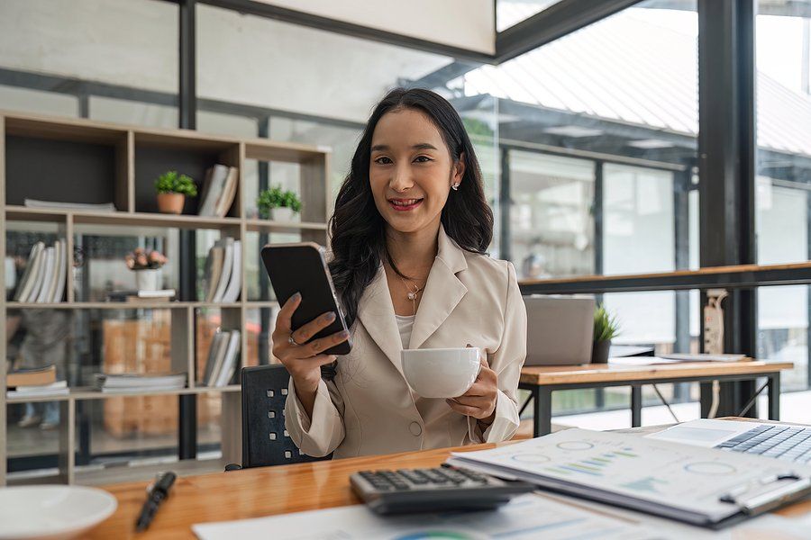 Woman holding phone and coffee smiles at the camera while looking at job boards