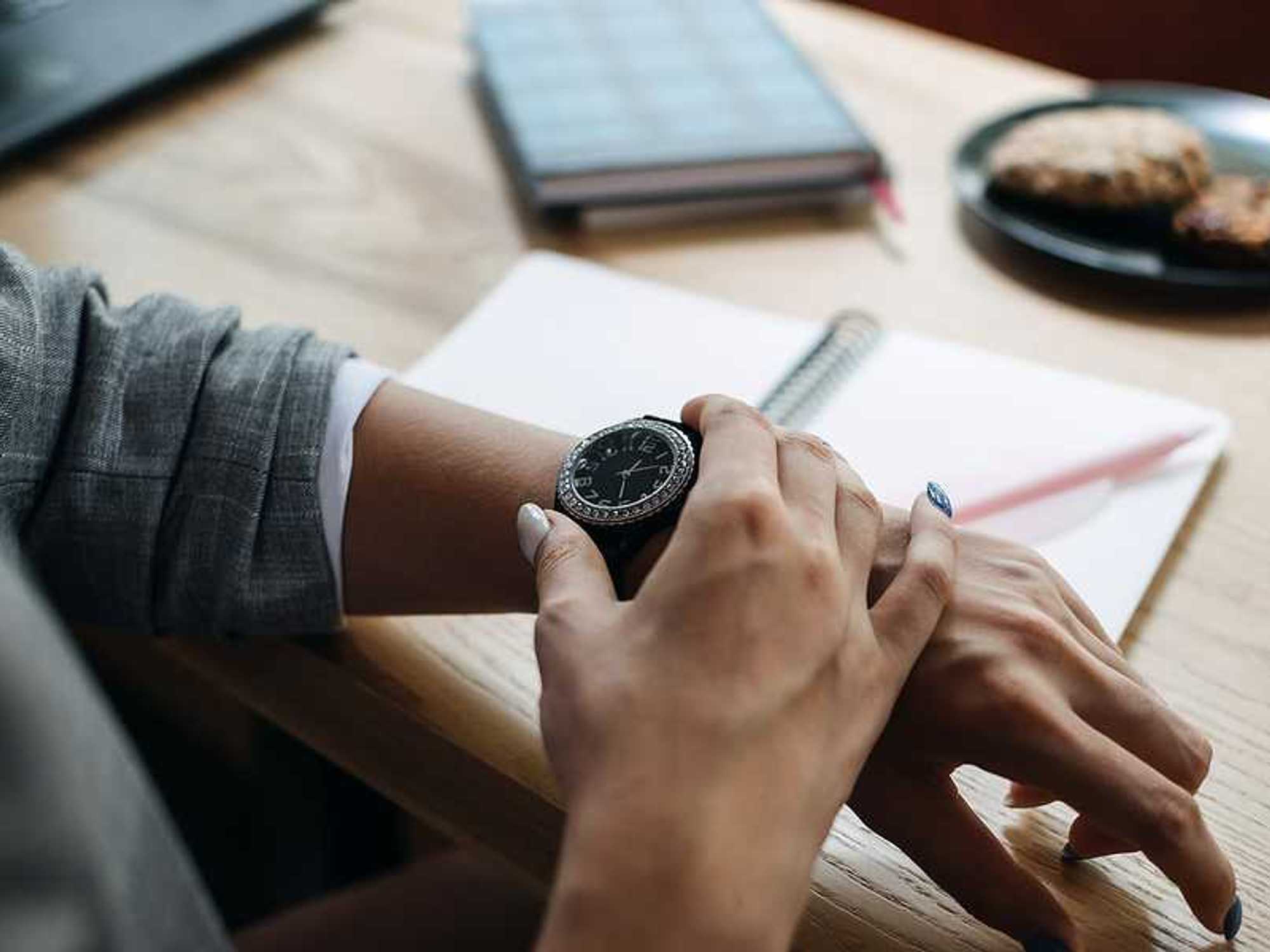 Woman looks at her watch while working, improving her time management with AI