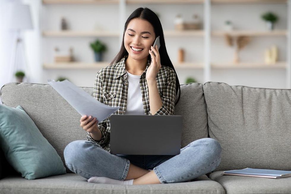 Wanita di laptop memegang resumenya sambil berbicara dengan manajer perekrutan di telepon