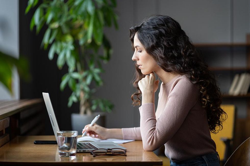 Woman on laptop improving her time management skills by writing down her priorities