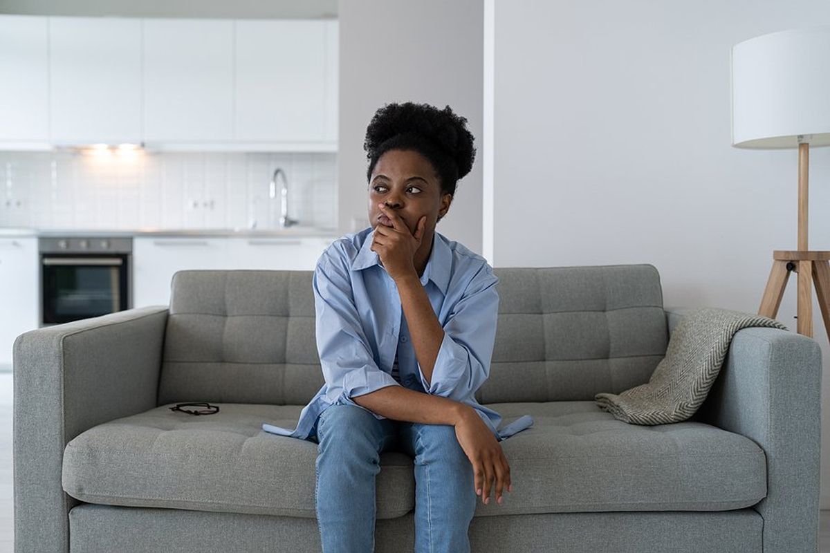 Woman sitting on couch thinks about and fears getting laid off
