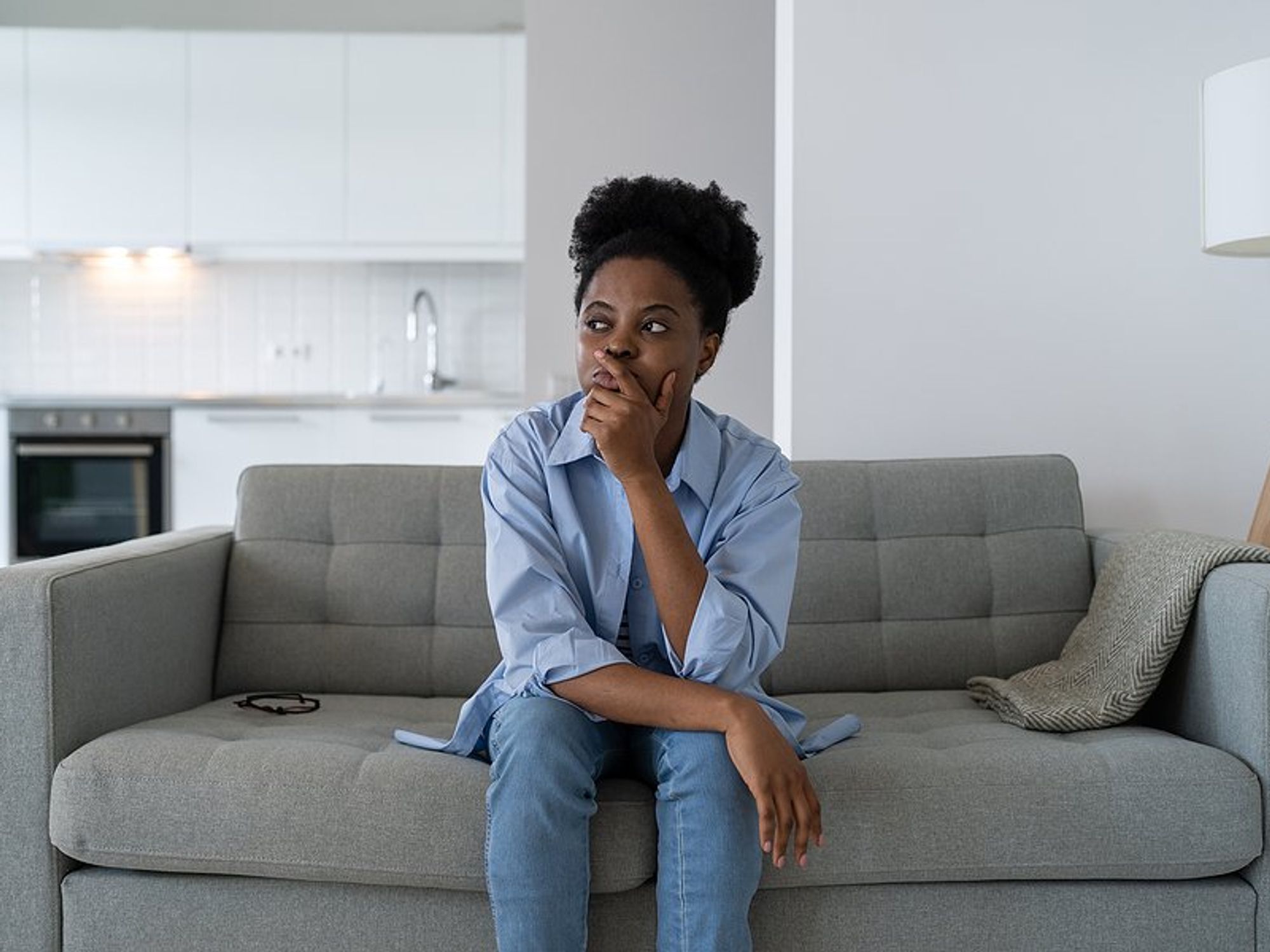 Woman sitting on couch thinks about and fears getting laid off