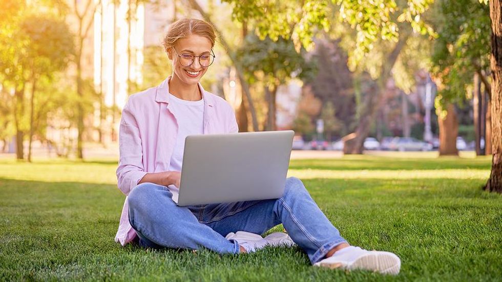 Woman sitting on the grass writes a thank you note on her laptop