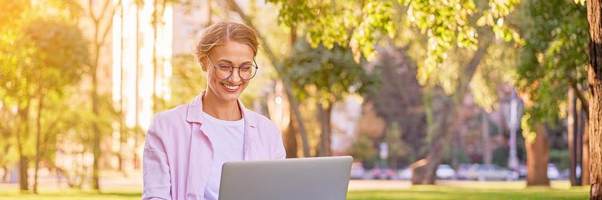 Woman sitting on grass types on her laptop