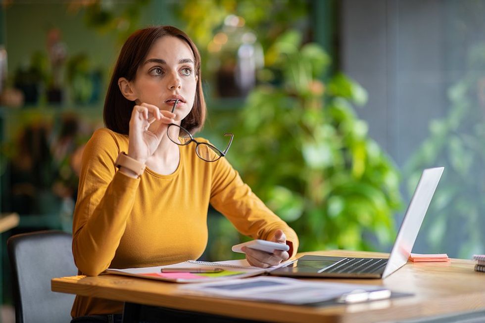 Woman thinking about a fake job posting while on her phone and using her laptop