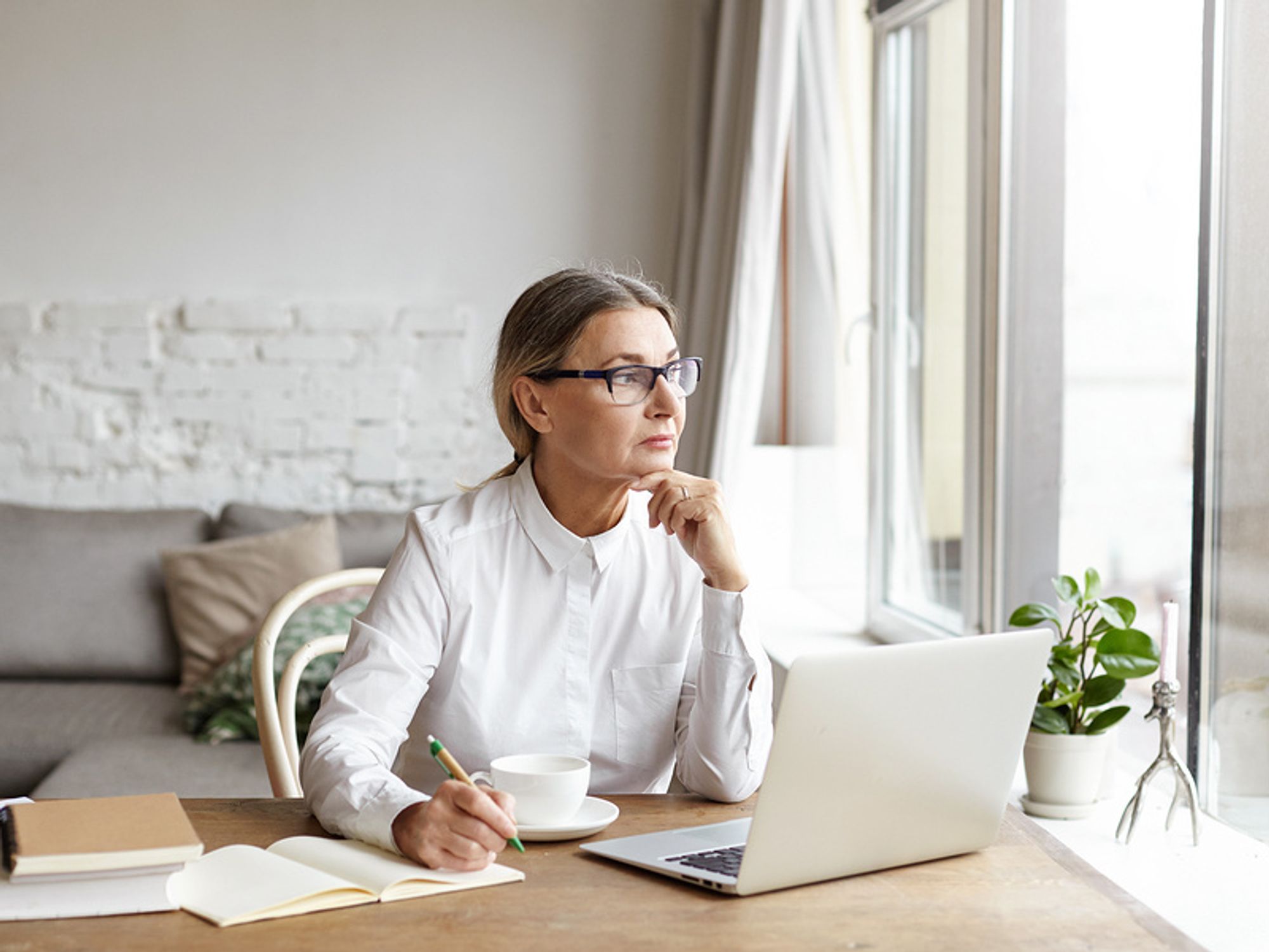 Worried woman in an office looking out the window debating whether she should get a better job.