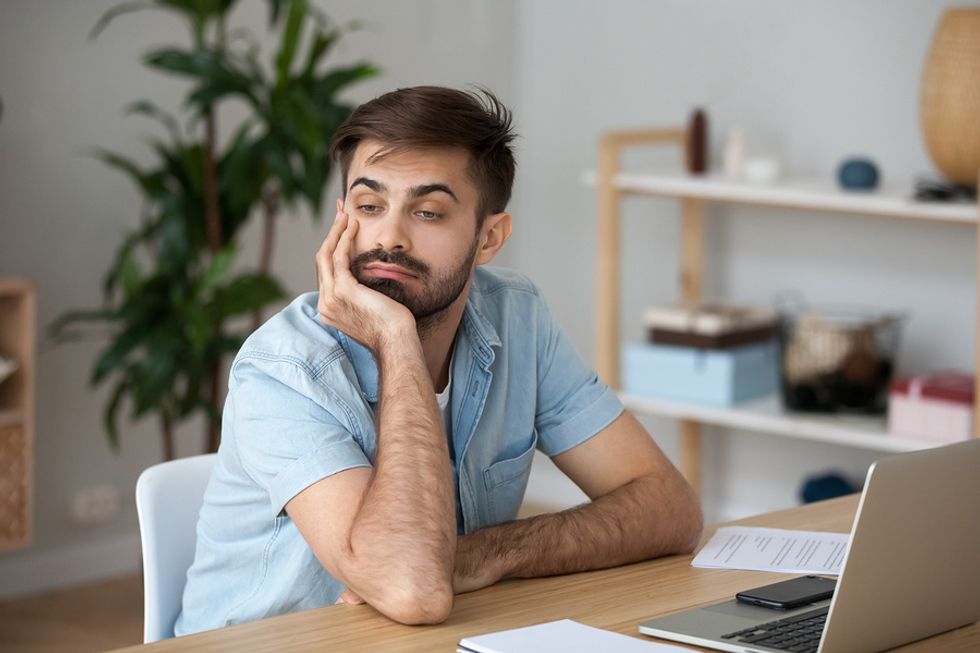Young man looking bored at his desk and deciding whether he should get another job