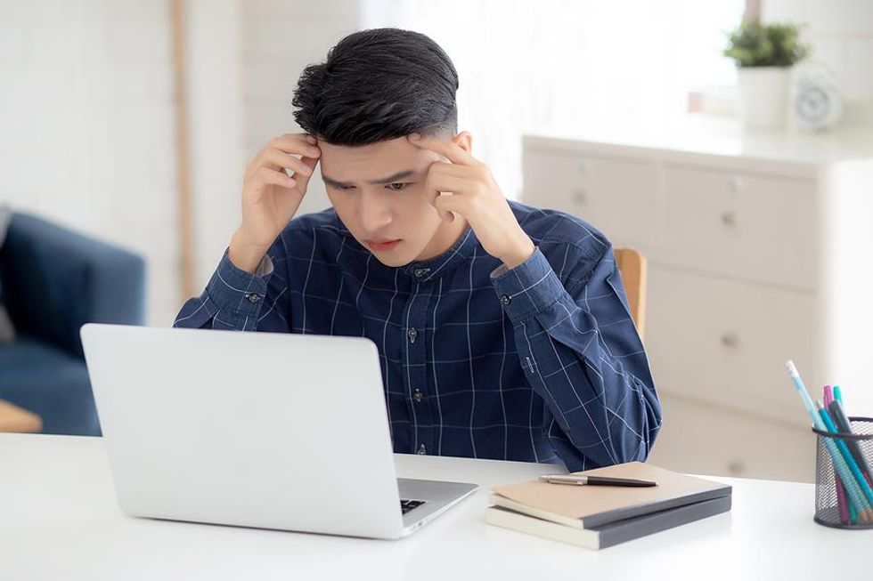 Young man on laptop feels miserable at work