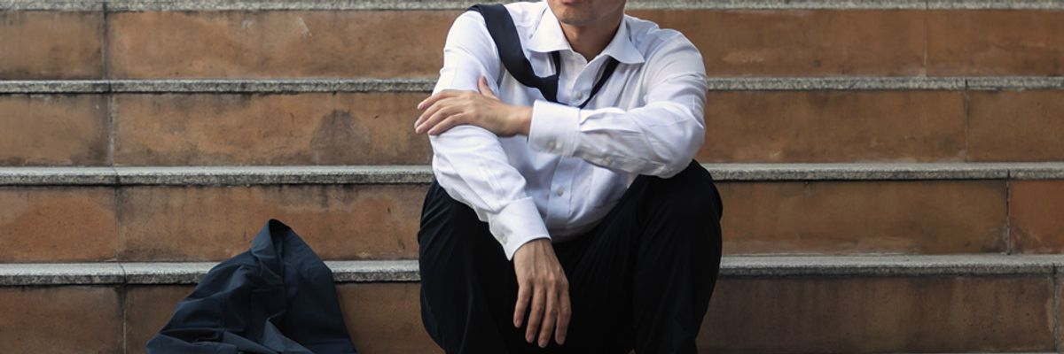 Young professional man sitting on steps, feeling upset that he's unemployed.