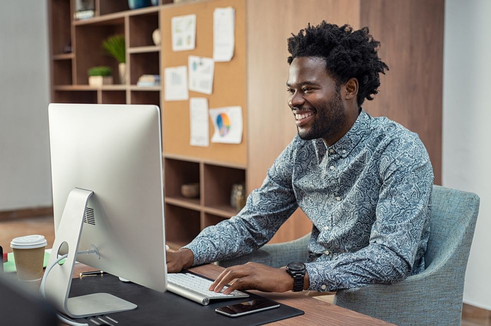 Young professional man smiling at his desk in an office feeling happier about his work situation