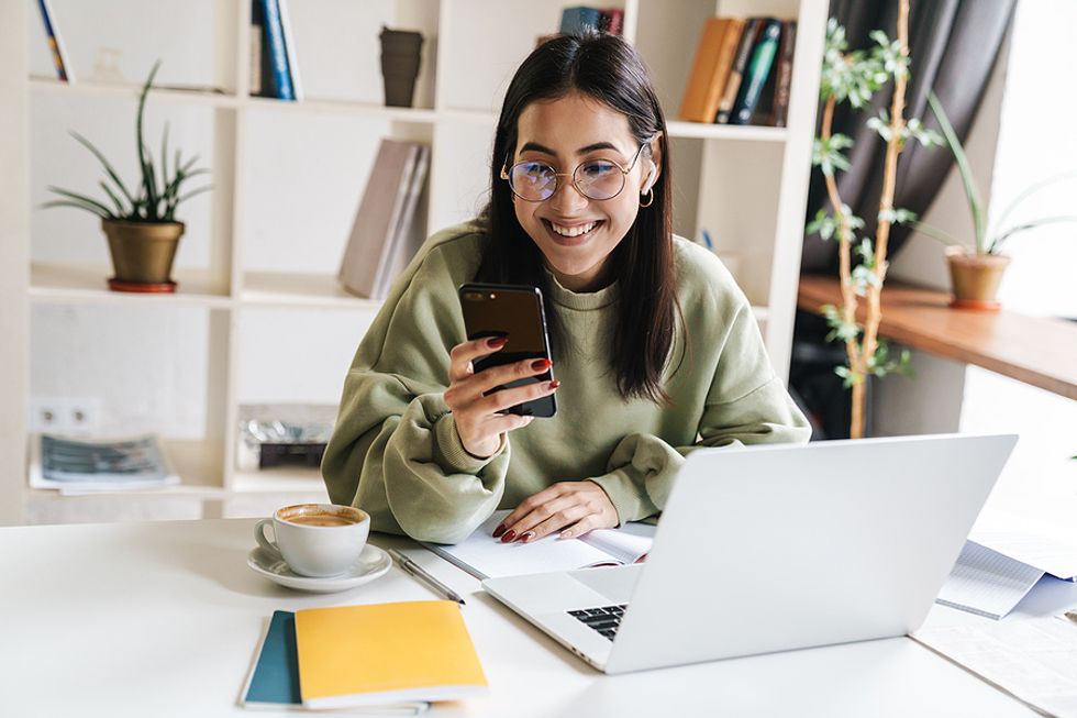 Young professional on phone and laptop finds out she got a job after college