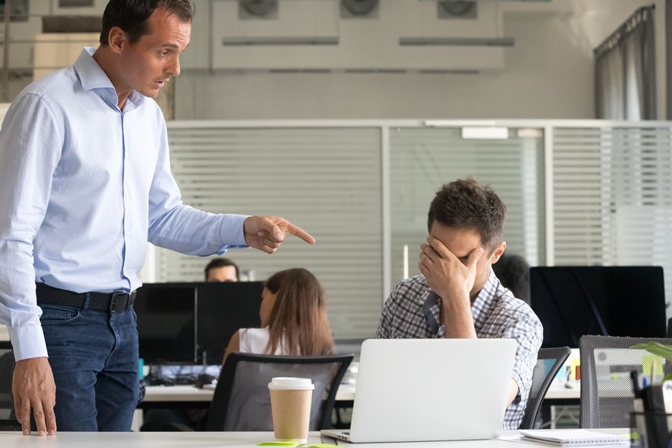 Young professional upset at his desk while his coworker yells at him