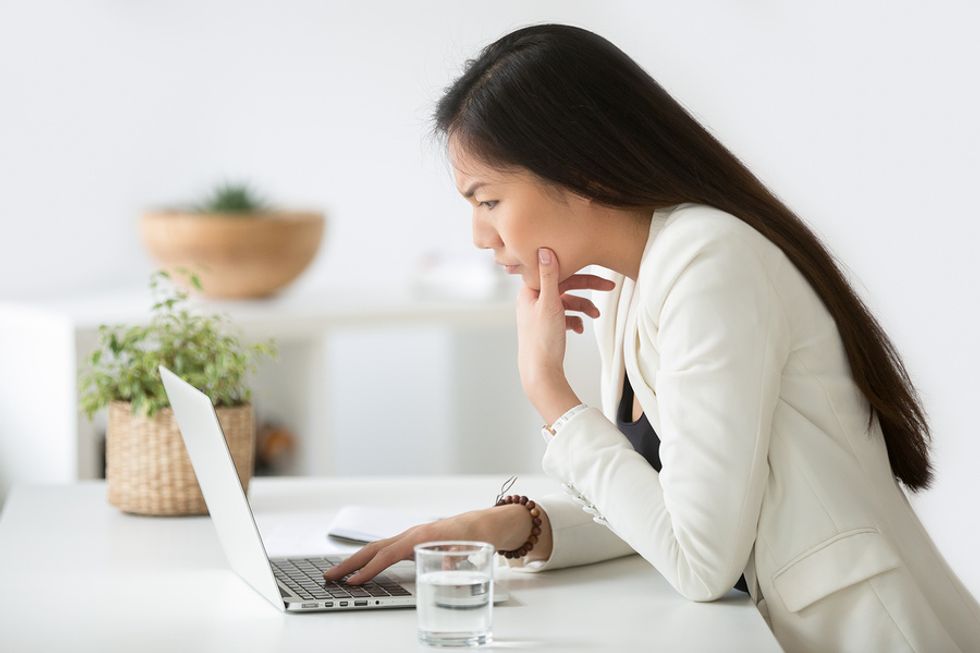 Young professional woman researching a company on her laptop to determine if she should turn down a job offer.