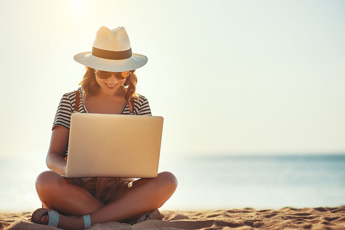 Young woman on laptop works on her resume while at the beach