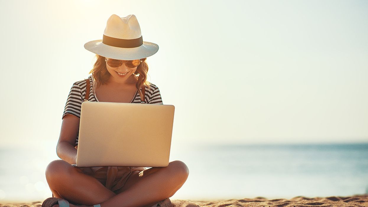 Young woman on laptop works on her resume while at the beach