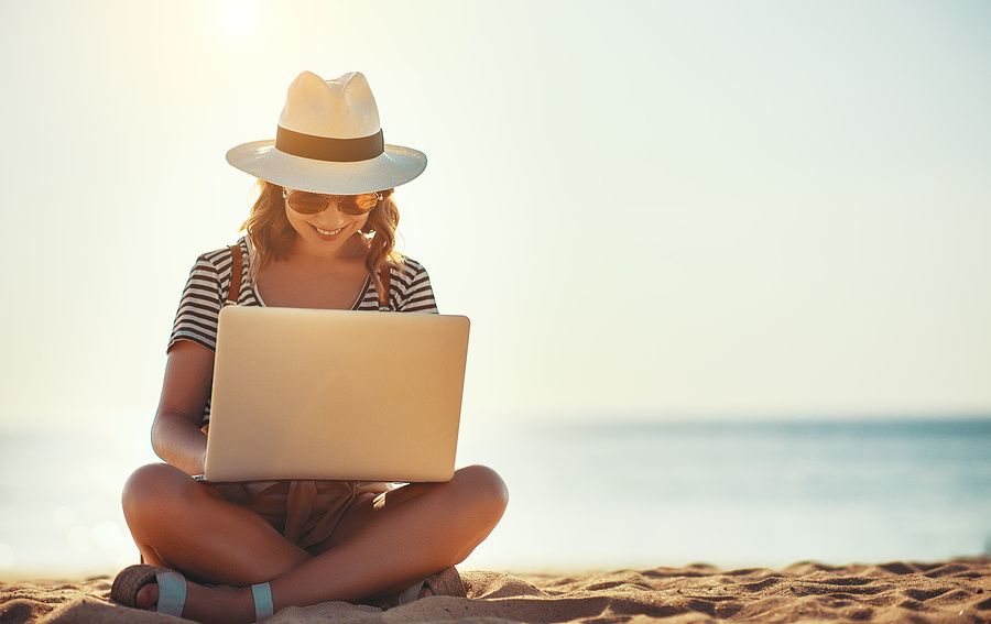 Young woman on laptop works on her resume while at the beach