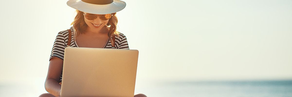 Young woman on laptop works on her resume while on the beach