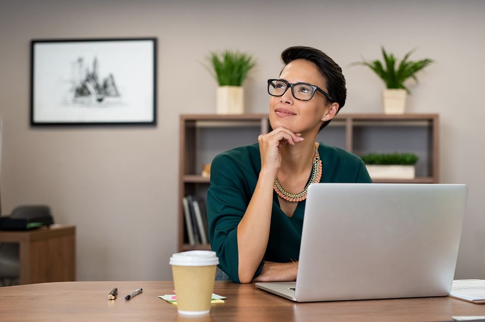 Young woman thinking positively about her work while working at her desk