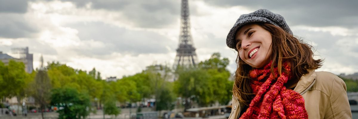 Young woman with a travel career smiling while standing on a bridge in Paris