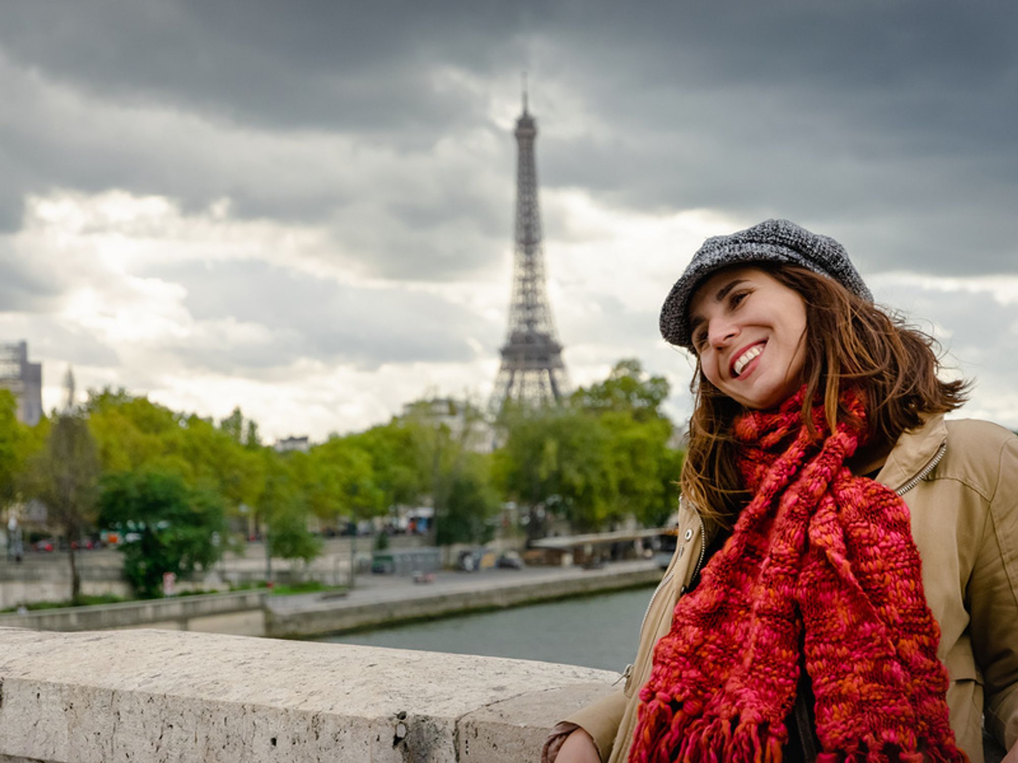 Young woman with a travel career smiling while standing on a bridge in Paris
